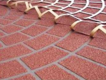 A close-up view of a red decorative concrete surface with a fan-shaped stencil pattern partially lifted to reveal the design. This is an example of how concrete stenciling is done.