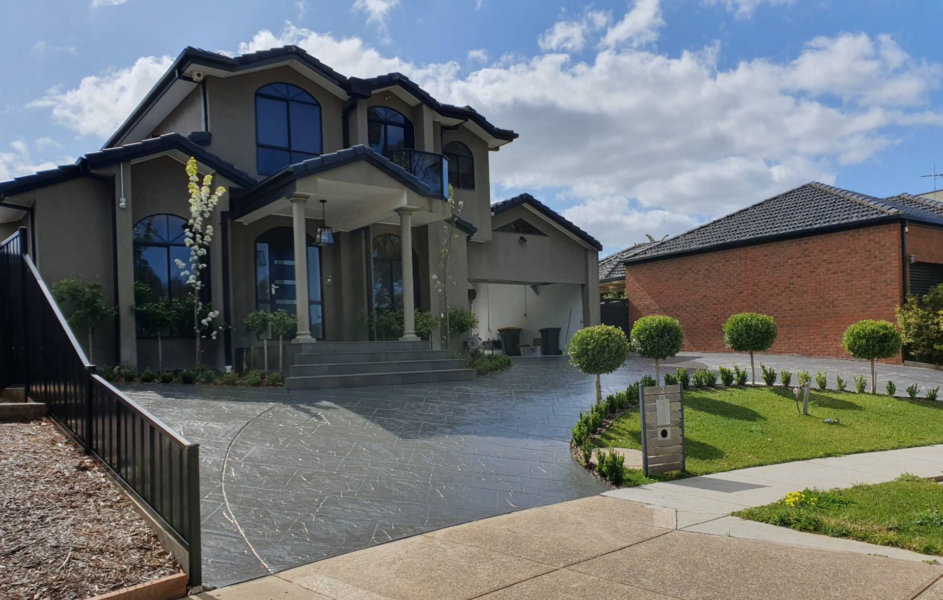 A beautifully resurfaced designer driveway leading to a grand home with manicured landscaping under a blue sky.
