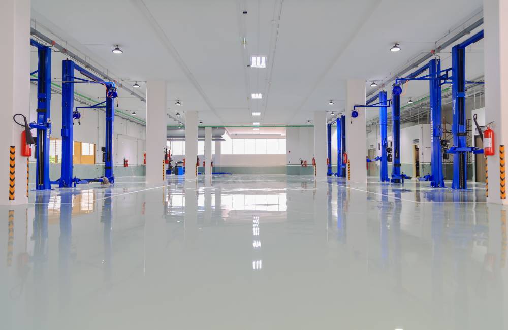 A clean, high-gloss epoxy floor in a large automotive workshop with car hoists and equipment.