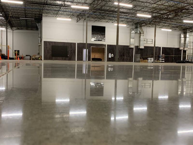 Polished concrete flooring in a spacious industrial facility with high ceilings and bright lighting reflecting off the incredibly shiny surface.
