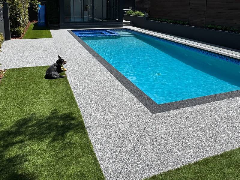 Decorative permeable paving around a residential pool with adjoining artificial turf and a dog resting nearby