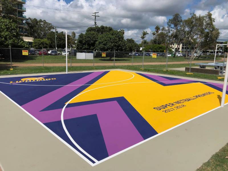 A custom-designed netball court with bright purple and yellow surfacing, team branding, and court markings.