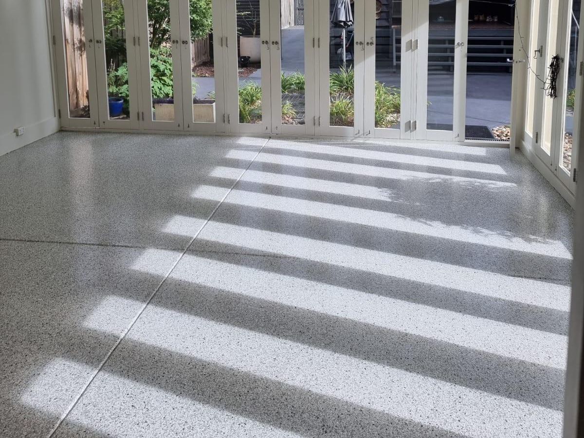 Light grey epoxy flake flooring in a bright sunroom with glass doors, offering a stylish and easy-to-clean finish.