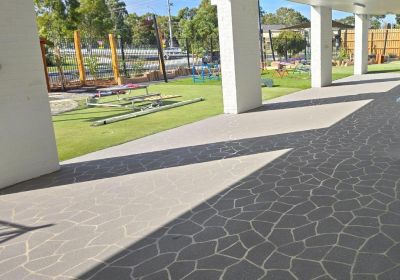 Light grey concrete floor with random stone stencil pattern in an outdoor covered walkway at a childcare facility, adjacent to play equipment and a grassy area.