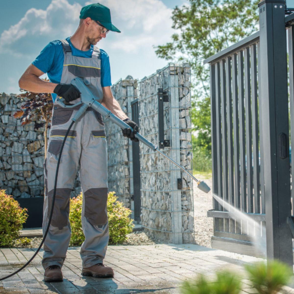 Worker using a high-pressure cleaning machine to wash a large metal gate in Melbourne.