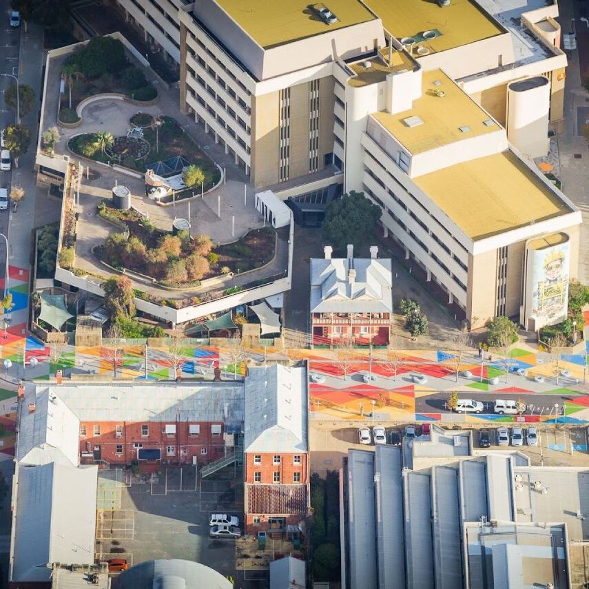 Aerial view of Melbourne CBD featuring vibrant, geometric-patterned asphalt coatings at multiple pedestrian crosswalks, showcasing the impact of decorative surface treatments on urban streetscapes