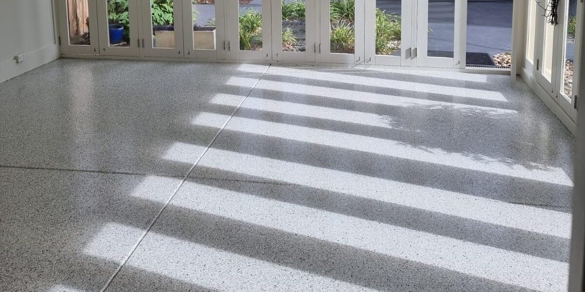 residential-sunroom-epoxy-flake-flooring-light-grey-spray-pave-melbourne Light grey epoxy flake flooring in a bright sunroom with glass doors, offering a stylish and easy-to-clean finish.
